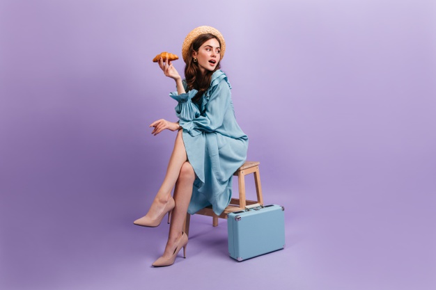 full-length-shot-young-lady-elegant-blue-dress-woman-sits-stool-suitcase-holds-delicious-croissant_197531-14322 (1)