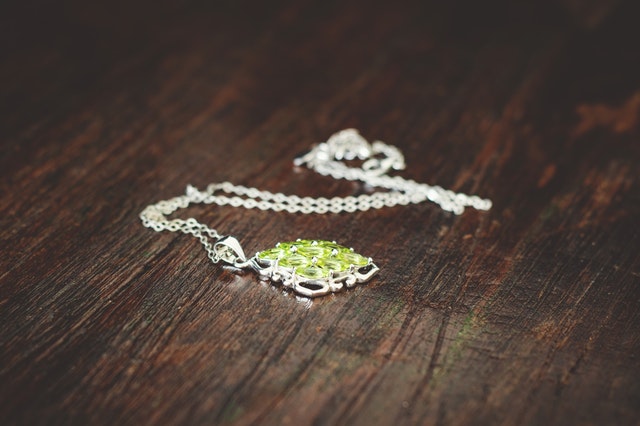 Strieborný  náhrdelník so zeleným kaňom na drevenom stole