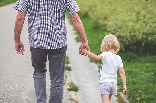 Starší muž kráča po chodníku a drží za ruku vnučku.jpg